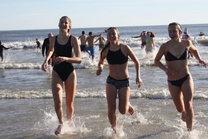 Plunge participants splash through the ocean waves with big grins.
